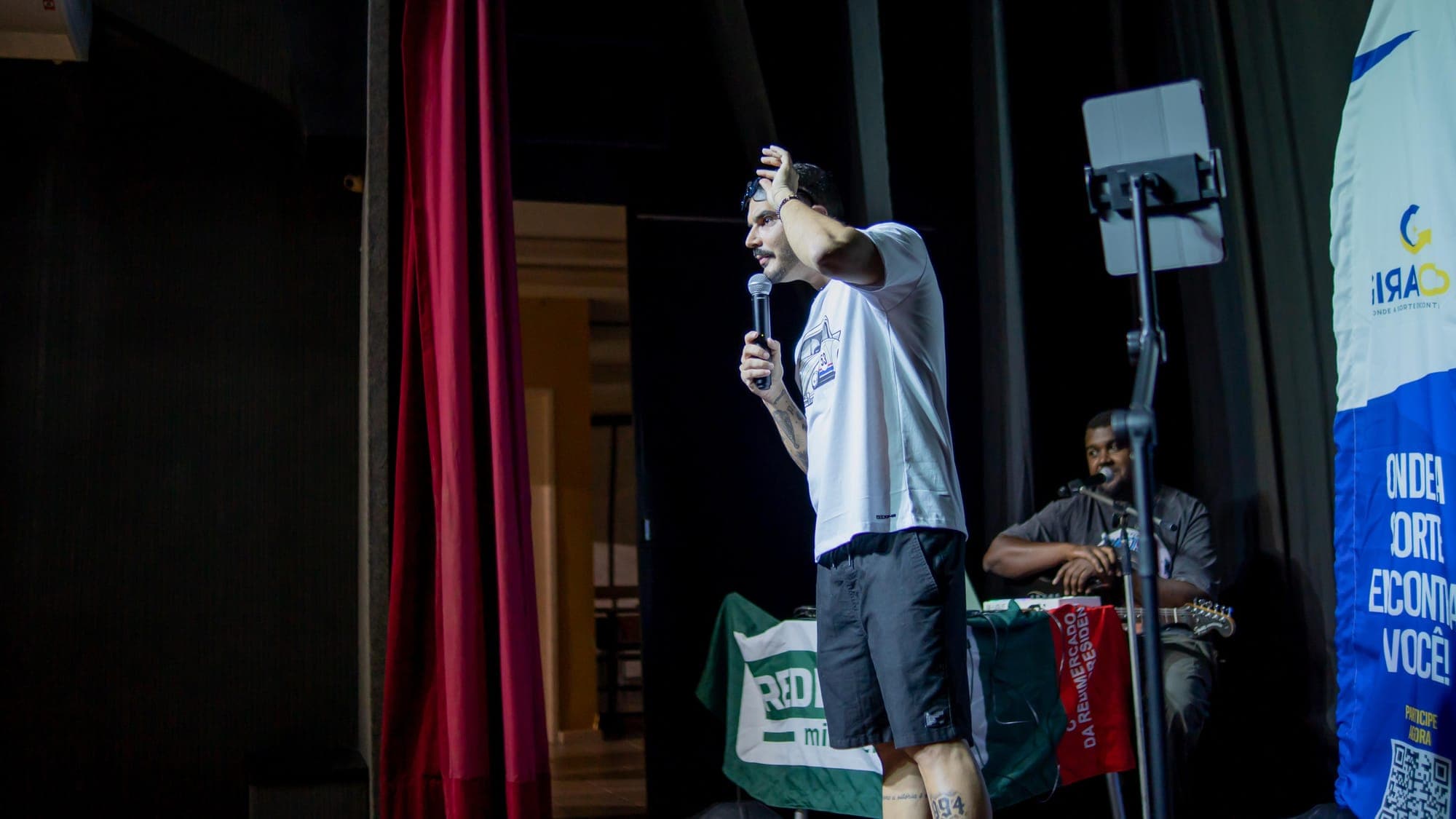 Igor com o microfone, levando a mão à cabeça no palco