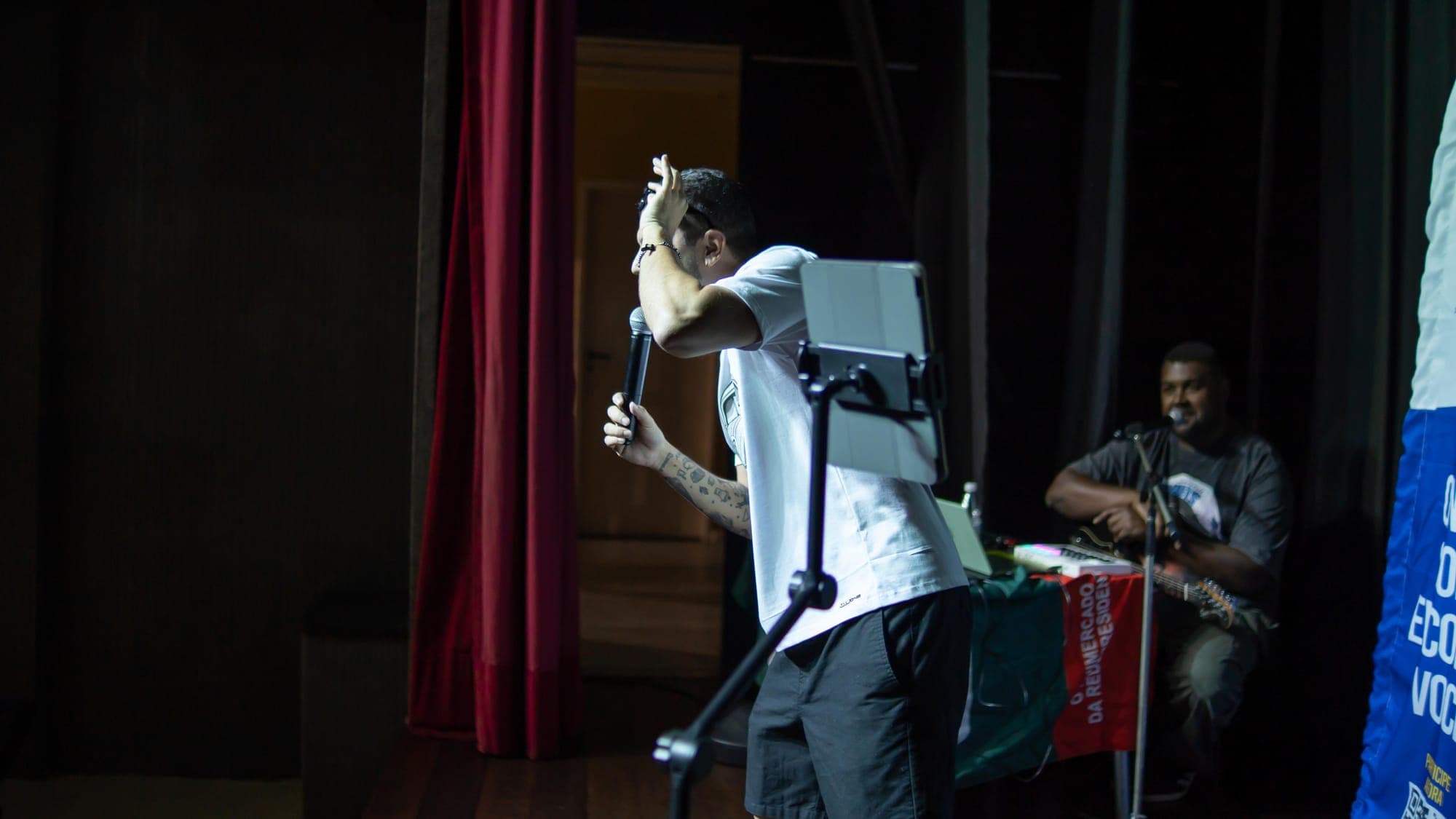 Igor no palco, de costas, com a mão na testa e o microfone na outra mão
